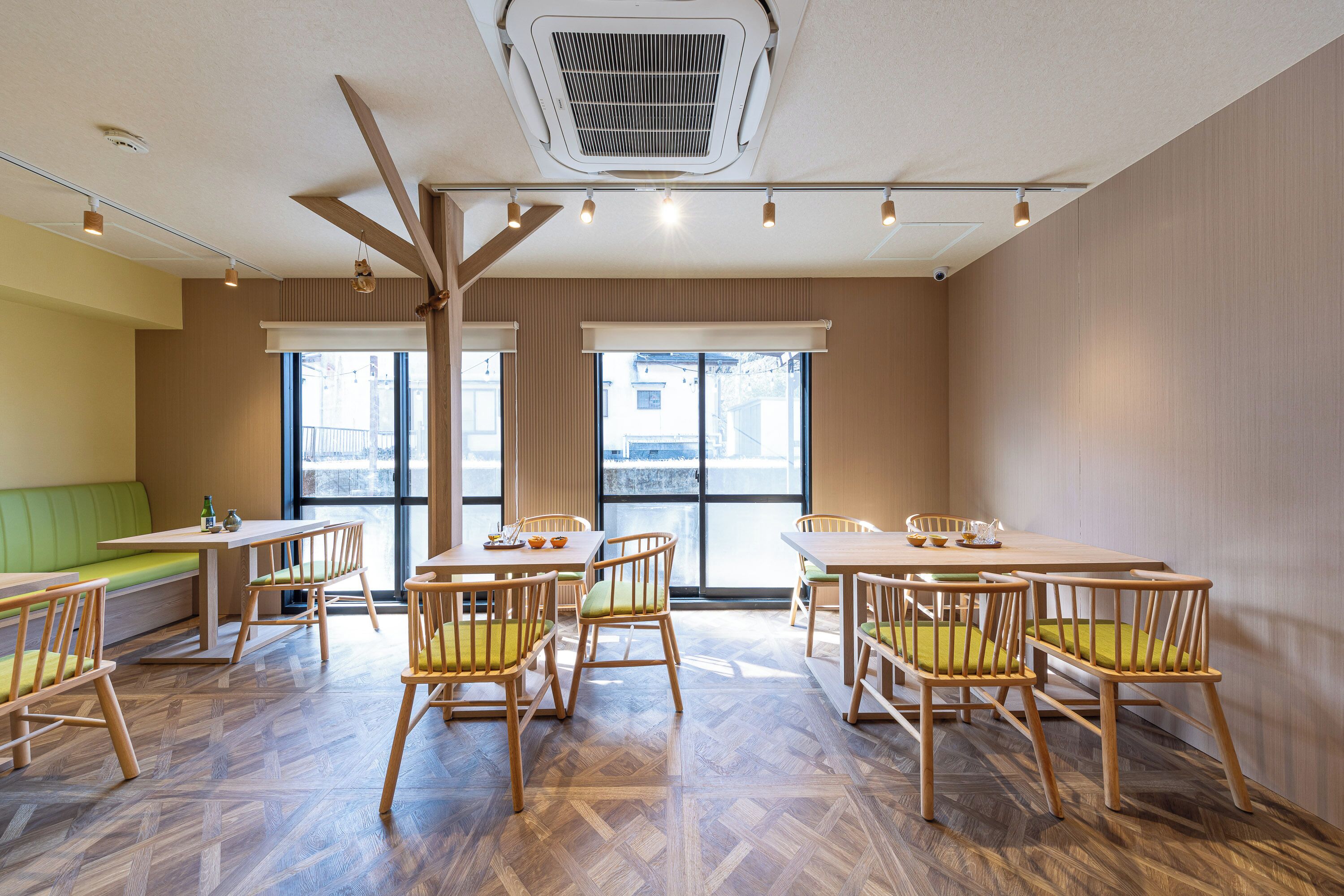 Un comedor con mesas y sillas de madera, un ventilador de techo y ventanas amplias.