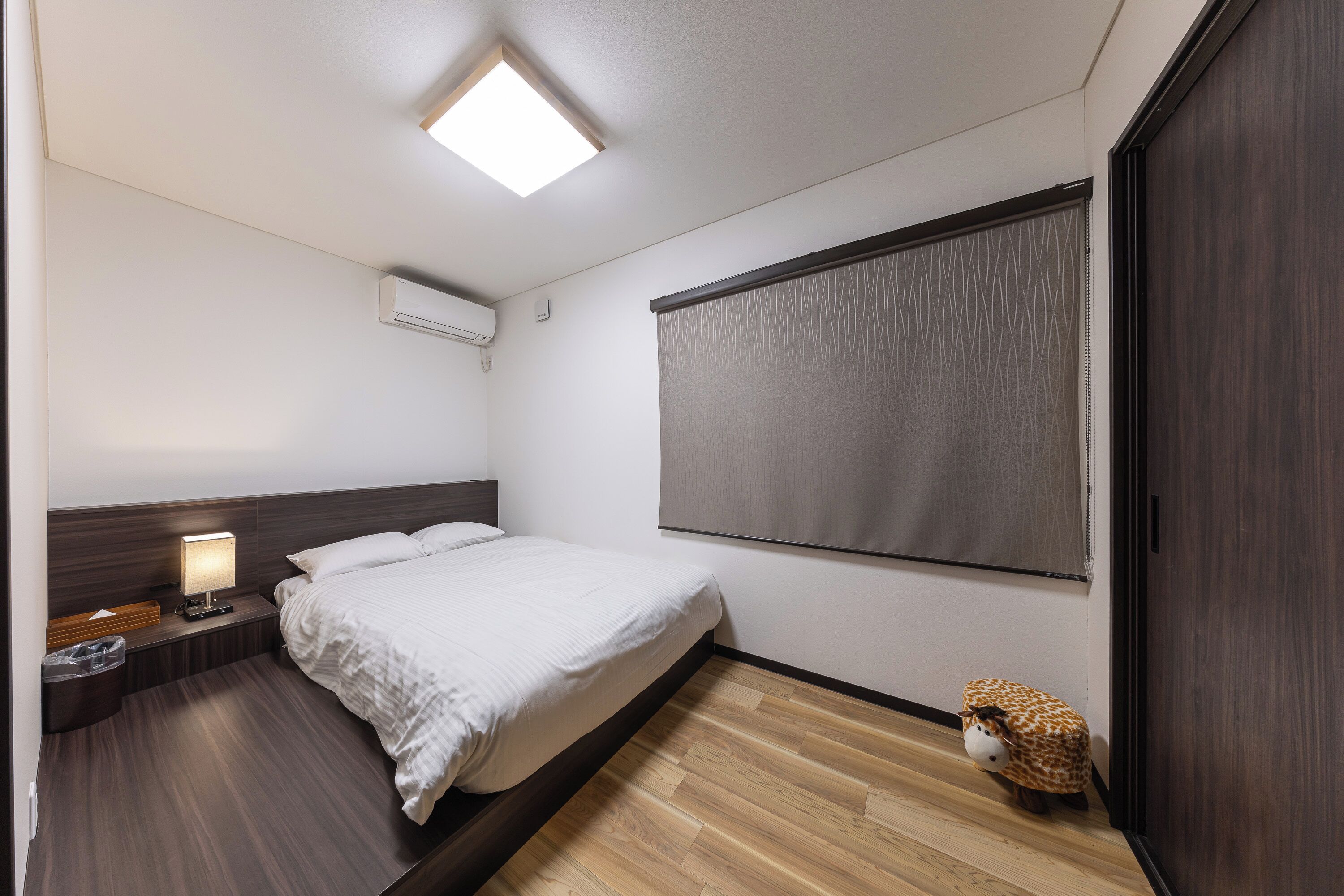 A bedroom with a bed, bedside table, lamp, and a small animal figure.