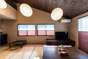 Una stanza con pavimento in tatami, un tavolino con una pianta, una televisione e una ventola a soffitto.