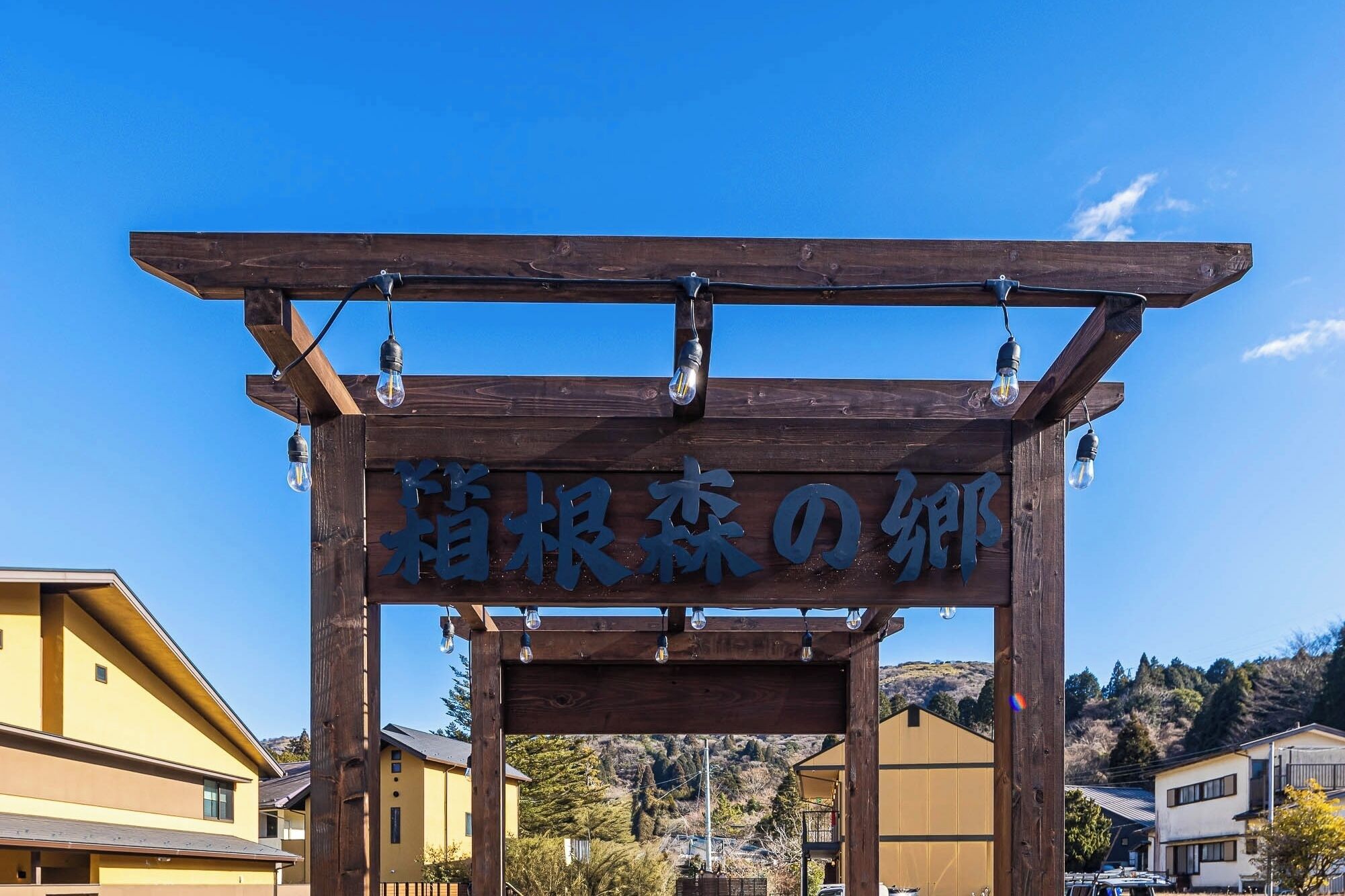 A wooden structure with a sign, possibly a gateway or entrance, with light bulbs hanging from it.