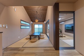 A hallway with tatami mats, a wooden table, and a television in the adjacent room. - Hakone Mori No Sato (Hakone)