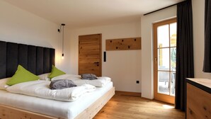 A modern bedroom with a wooden bed, a large window, and a wooden wall panel. - "Nock" | ZumMoarSepp - Holiday apartment in the Villnöss Valley (Trentino-Alto Adige)