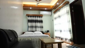 A bedroom with a bed, a table, a ceiling fan, an air conditioning unit, and a window with curtains. - Kishoreganj Haor Resort (Kishoreganj Sadar)