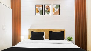 Ein modernes Schlafzimmer mit einem Holzkopfende, zwei schwarzen Kissen, einer weißen Bettdecke und drei gerahmten Kunstwerken an der Wand.
