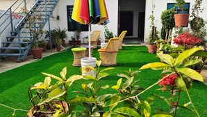 Een terras met kunstgras, rieten stoelen en potplanten.