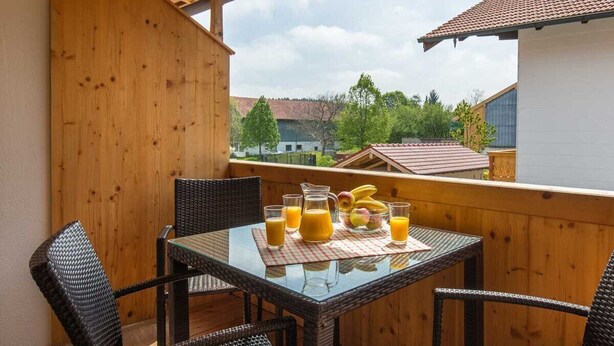 En balkon med et bord dækket til to personer, med en kande appelsinjuice, et glas appelsinjuice og en skål med frugt.