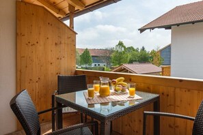 Un balcon avec une table dressée pour deux personnes, agrémentée d’une carafe de jus d’orange, d’un verre de jus d’orange et d’un saladier de fruits.