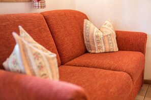 A red sofa with floral patterned pillows. - Vacation apartment Magdalena (Chieming)