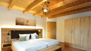 A bedroom with a wooden bed, a nightstand, a bench, a wardrobe, and a ceiling light fixture. - Vacation apartment Barbara (Chieming)