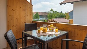 A wooden balcony with a table set for breakfast, including a pitcher of orange juice and a bowl of fruit. - Vacation apartment Barbara (Chieming)