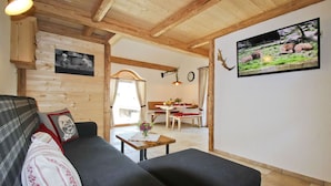 Una sala de estar acogedora con un sofá, una pequeña mesa con un florero y un televisor en la pared.