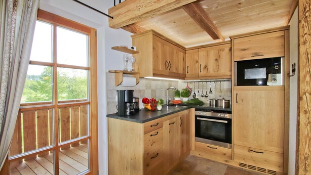 Una cocina con armarios de madera, encimera negra y un ventanal con vistas a la vegetación.