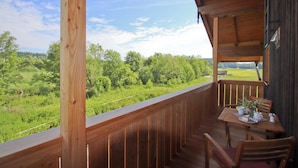 Una terraza de madera con mesa y sillas, con vista a un paisaje verde.