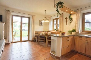 A kitchen with a dining area, large windows, and a cross on the wall. - Maria Vacation Rental – Accessible Family Apartment with a South-Facing Terrace and Garden (Chieming)