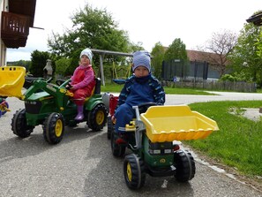 Two children riding toy tractors on a paved path. - Maria Vacation Rental – Accessible Family Apartment with a South-Facing Terrace and Garden (Chieming)