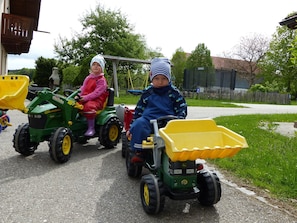 Två barn som åker på leksakstraktorer på en asfalterad stig.
