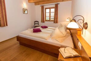 Ein Schlafzimmer mit einem hölzernen Bett, zwei Kissen, einem Nachttisch mit Lampe und einem Fenster mit Vorhängen.