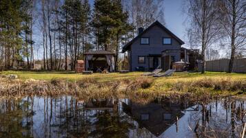 A house with a pond in front, surrounded by trees.