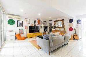 A living room with a sofa, TV, and various wall decorations. - Spacious 1BDR in St Kilda Near Tram and Beach (St Kilda)