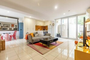 A modern living room with a sofa, coffee table, and red chairs. There is a kitchen area with cabinets and a refrigerator. - Spacious 1BDR in St Kilda Near Tram and Beach (St Kilda)