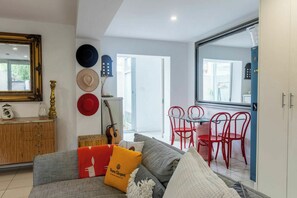 Un salon avec un canapé gris, des fauteuils rouges, une table à manger et une grande fenêtre.
