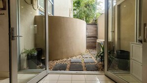 Een modern interieur met een gebogen muur, glazen deuren en een betegelde vloer die leidt naar een buitenruimte met een tuin.