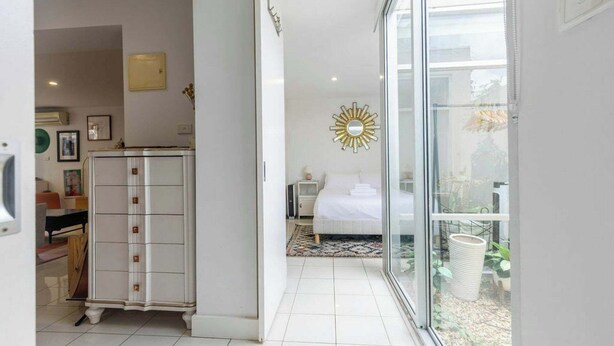 Een slaapkamer met een bed, nachtkastje, dressoir en een groot raam.