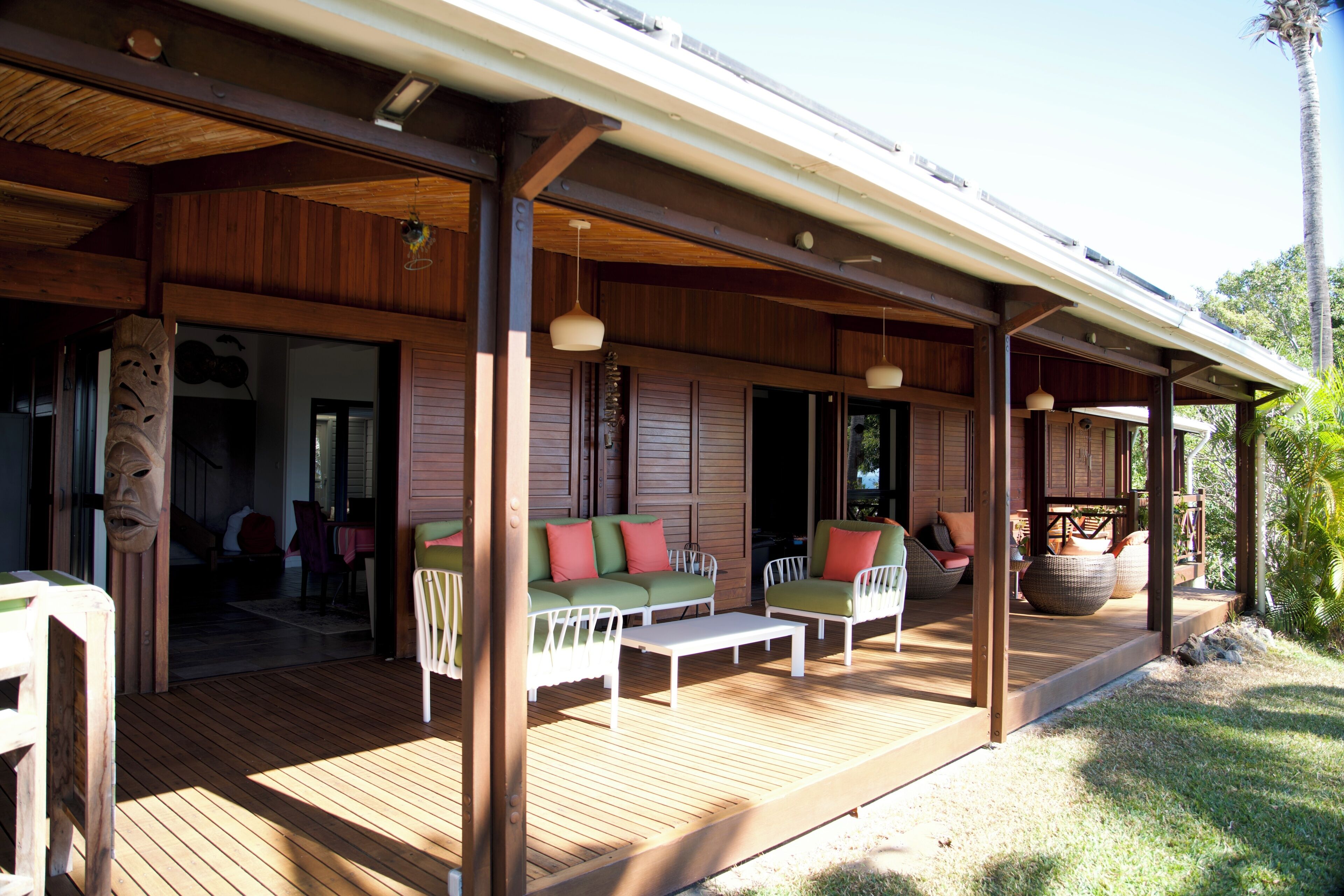 An outdoor covered patio with wooden flooring, seating arrangements, and a view of the surrounding greenery.