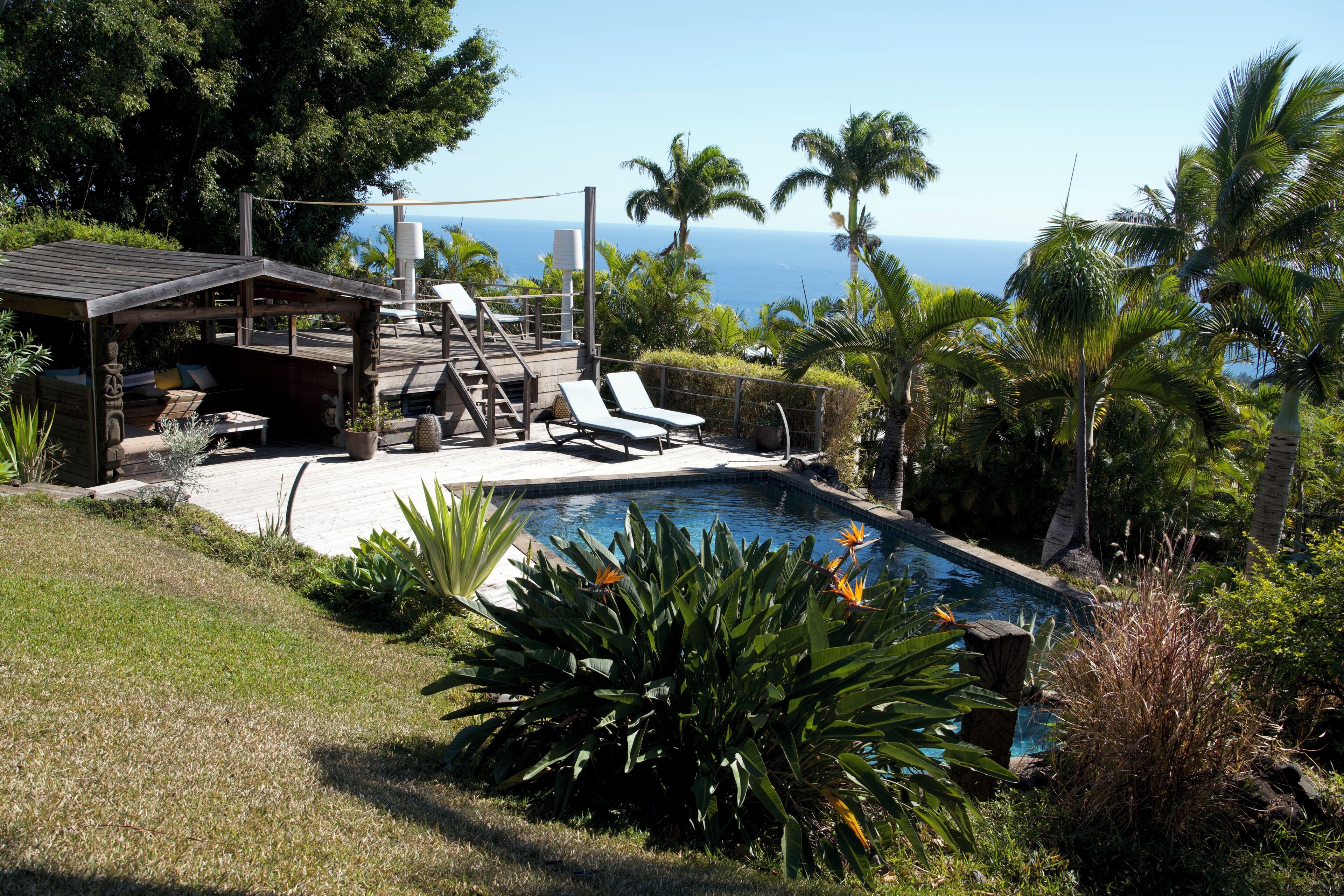A pool area with lounge chairs, a wooden deck, and a view of the ocean.