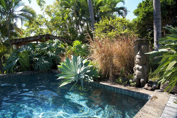 A swimming pool surrounded by tropical vegetation and a stone statue. - Villa Maido Luxe (Saint-Paul)