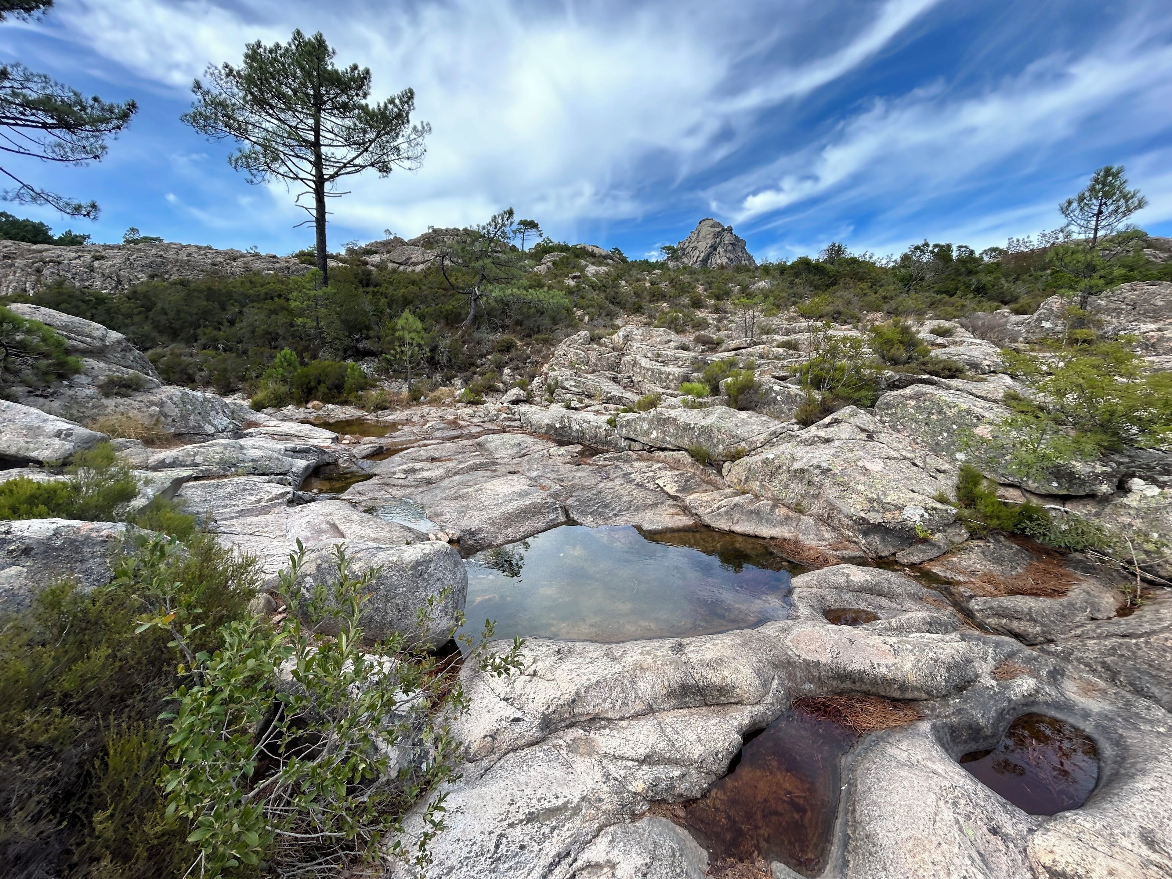 Un paysage rocheux avec un petit étang, entouré d’une végétation clairsemée, sous un ciel dégagé.