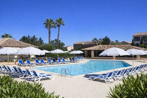 A poolside area with blue lounge chairs and white umbrellas, surrounded by palm trees and buildings with tiled roofs. - Walking distance to beaches - 2 swimming pools - Shaded terrace - Ideal for vacations (Linguizzetta)