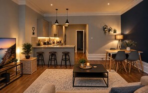 A modern living room with a kitchen area, bar stools, a dining table, and a TV. - Steps from Beach & Lanes | Stylish Brighton (Brighton and Hove)