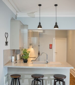 A modern kitchen with a central island, bar stools, pendant lighting, and a built-in sink. - Steps from Beach & Lanes | Stylish Brighton (Brighton and Hove)