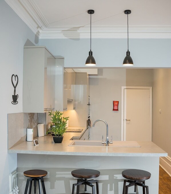 A modern kitchen with a central island, bar stools, pendant lighting, and a built-in sink. - Steps from Beach & Lanes | Stylish Brighton (Brighton and Hove)