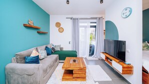 Una sala de estar moderna con sofá, mesa de centro, televisor y vistas al exterior.