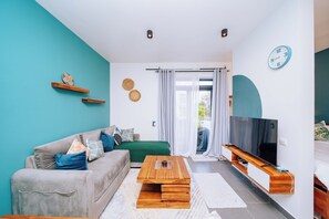 Una sala de estar moderna con sofá, mesa de centro, televisor y vistas al exterior.