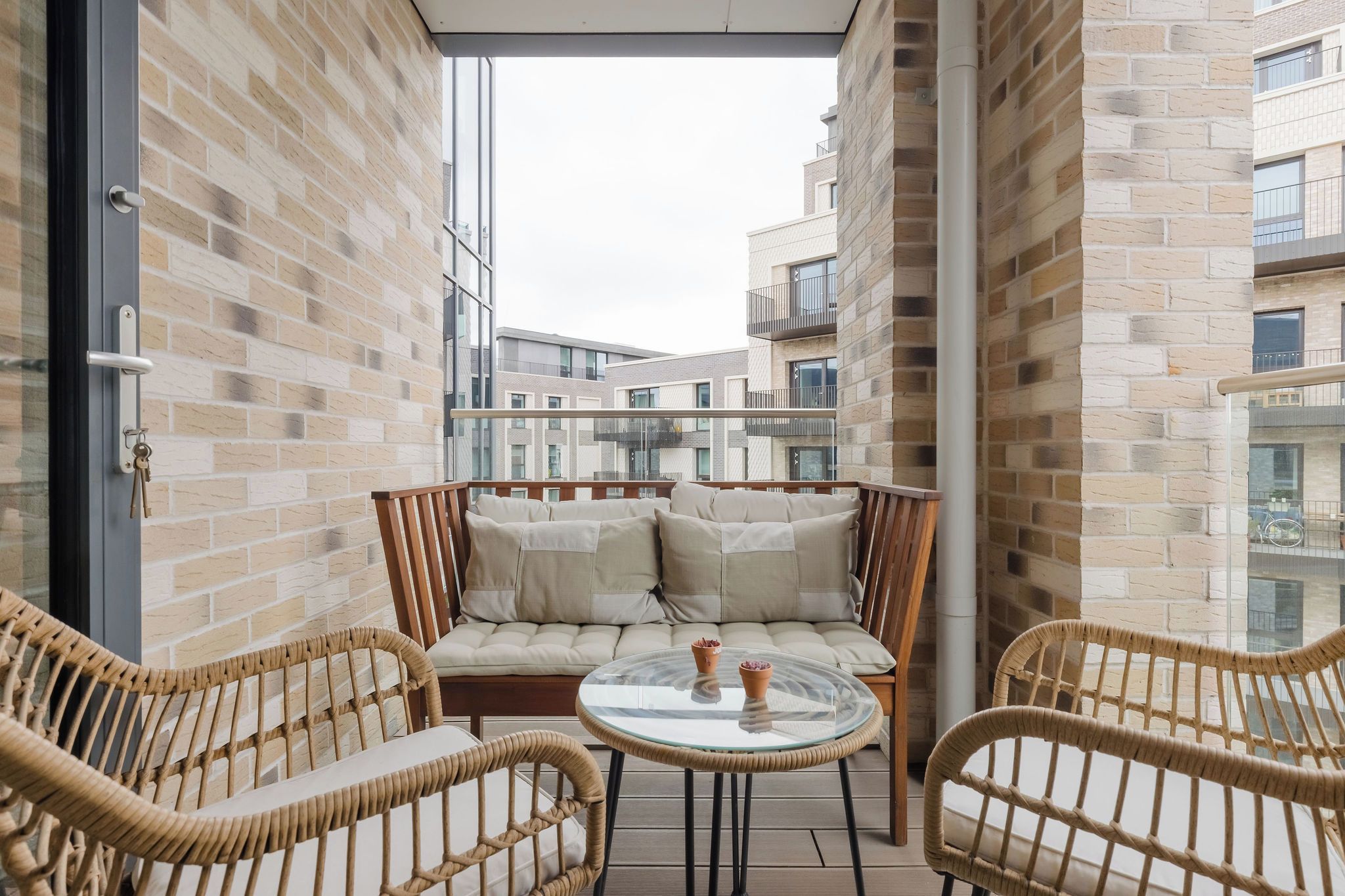 A balcony with wicker chairs, a glass table, and a cushioned sofa.