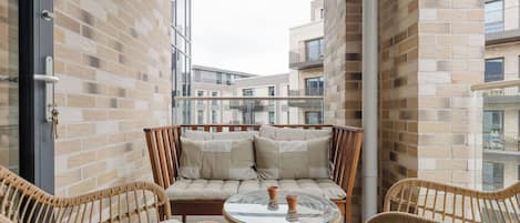 A balcony with wicker chairs, a glass table, and a cushioned sofa.