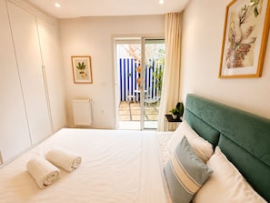 Quarto com cama, radiador, janela e porta que dá para uma área externa.