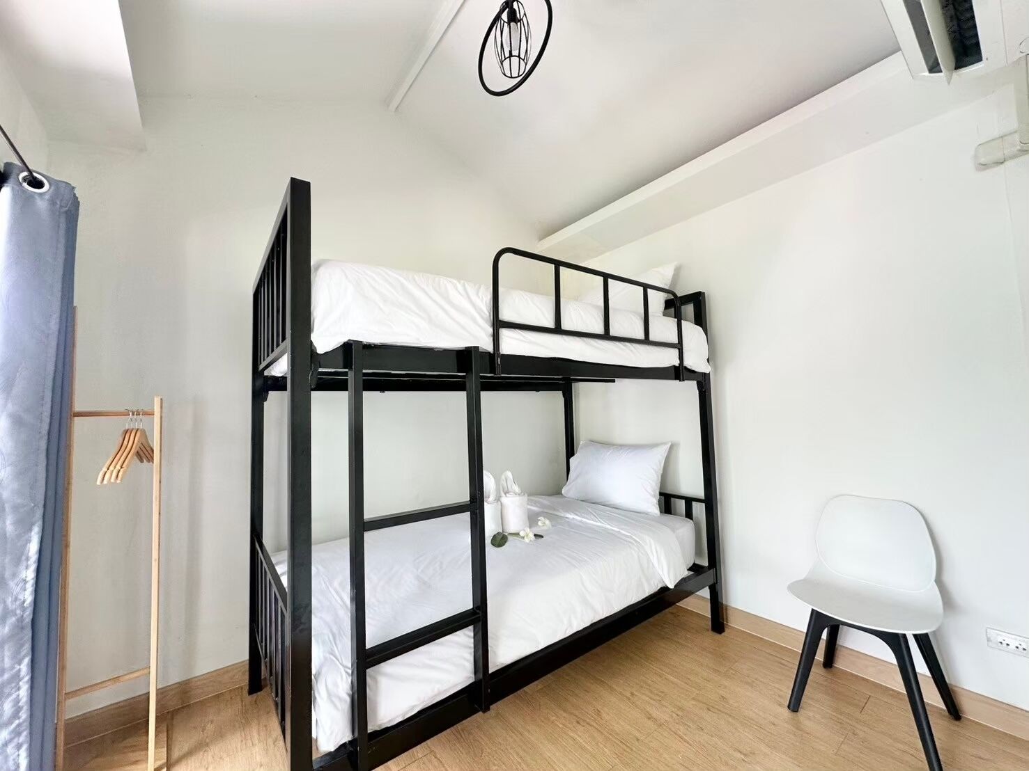 A bunk bed room with a wooden floor, a white chair, and a clothing rack.