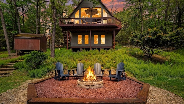 Eine Hütte mit einer Terrasse, einem Feuerkorb und umgebender Bepflanzung.