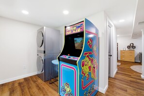 A laundry room with a washing machine, a dryer, and a colorful arcade game machine.