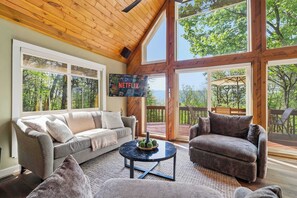 A cozy living room with a sofa, armchair, and coffee table, large windows, and a TV mounted on the wall. - Views of Blue Mountain! Near App Trail, Game Room (Palmerton)