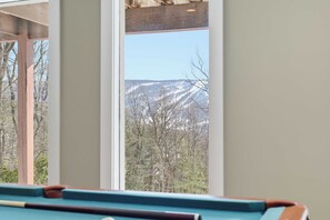 Una mesa de billar con vistas a un paisaje montañoso nevado a través de una ventana.