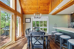 A dining area with a wooden ceiling, large windows, and a view of the outdoors.