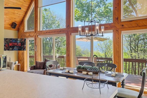 A spacious room with large windows, a dining area with a table set for two, and a television displaying the Netflix logo.