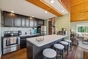 A modern kitchen with dark cabinets, stainless steel appliances, and a central island with stools.