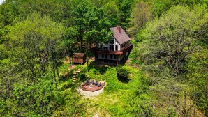 Ein Haus, umgeben von dichtem Wald, mit einer Terrasse und Sitzgelegenheiten im Freien.