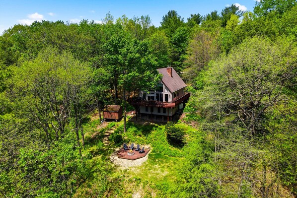 A house surrounded by dense forest, with a deck and outdoor seating area.
